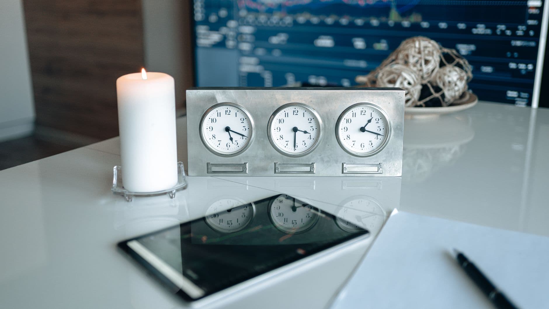 Workspace featuring a candle, world clocks, and a tablet with reflections on a shiny desk.