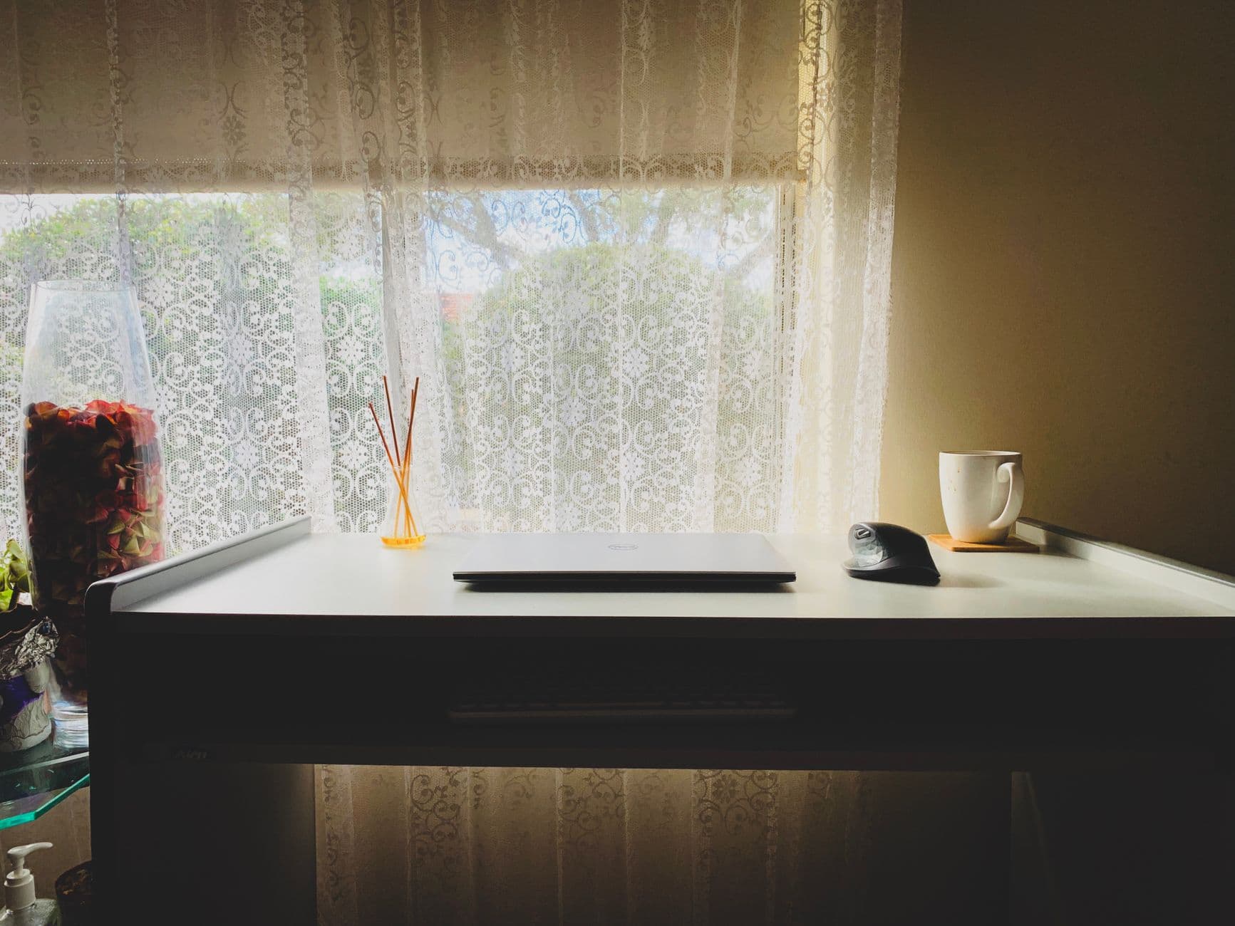 A modern minimalist desk setup with a laptop, mouse, and a mug by a window. Ideal workspace inspiration.