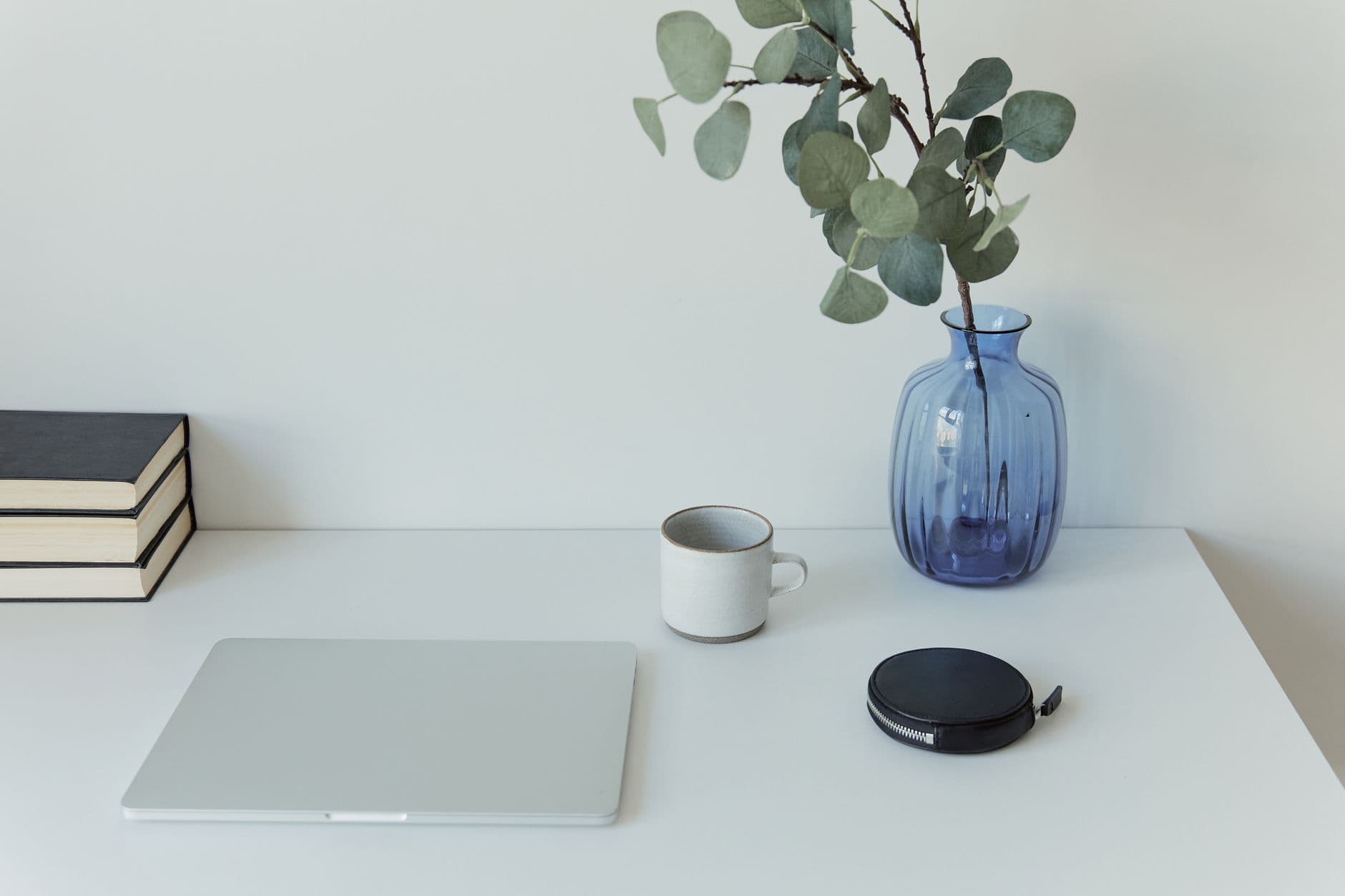 Clean minimalist desk featuring a laptop, blue vase with plant, and coffee mug.