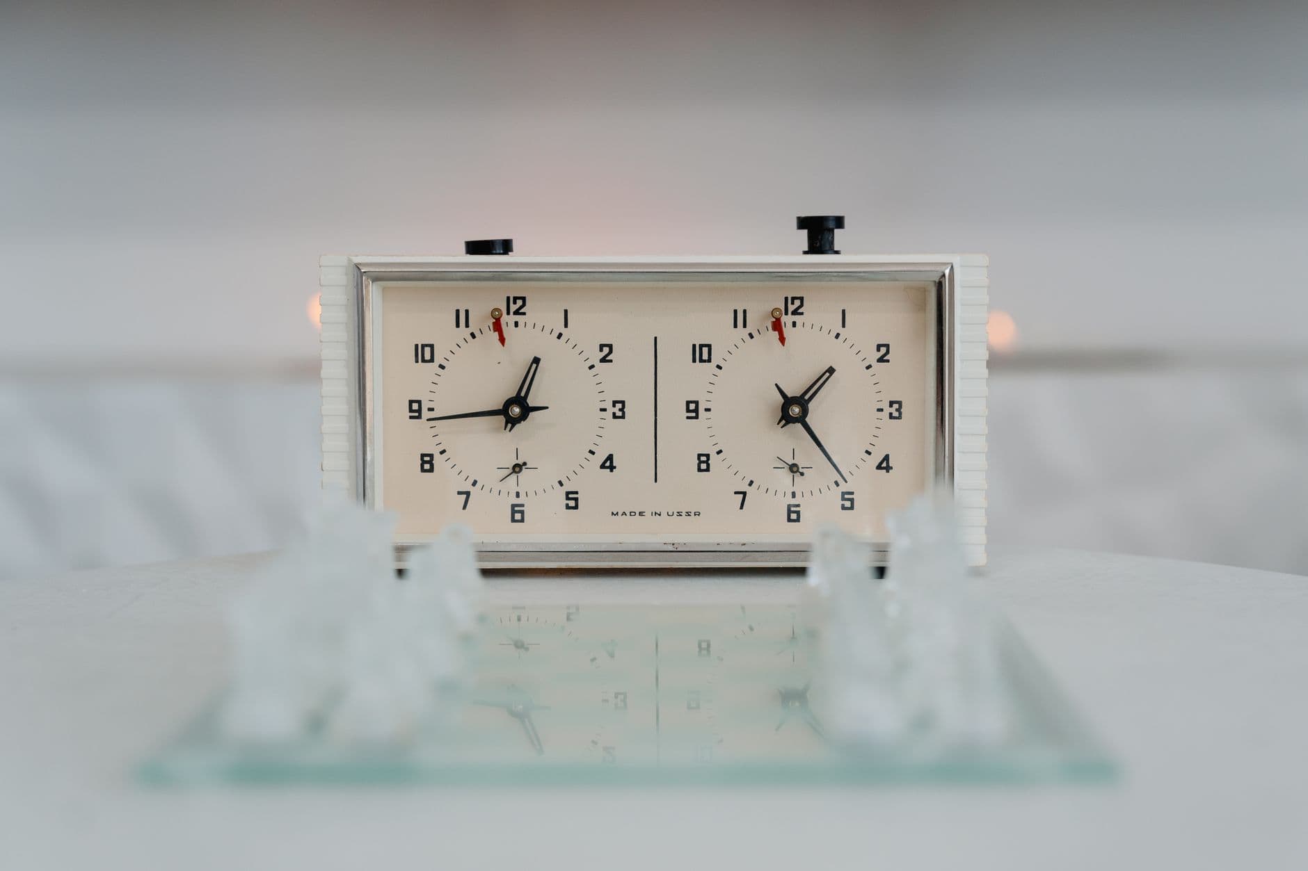 A vintage chess clock with blurred chess pieces in a close-up still life composition.