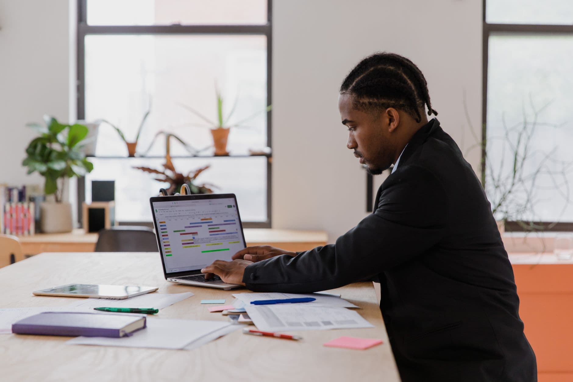 Businessman with braided hair focused on laptop work at office desk.