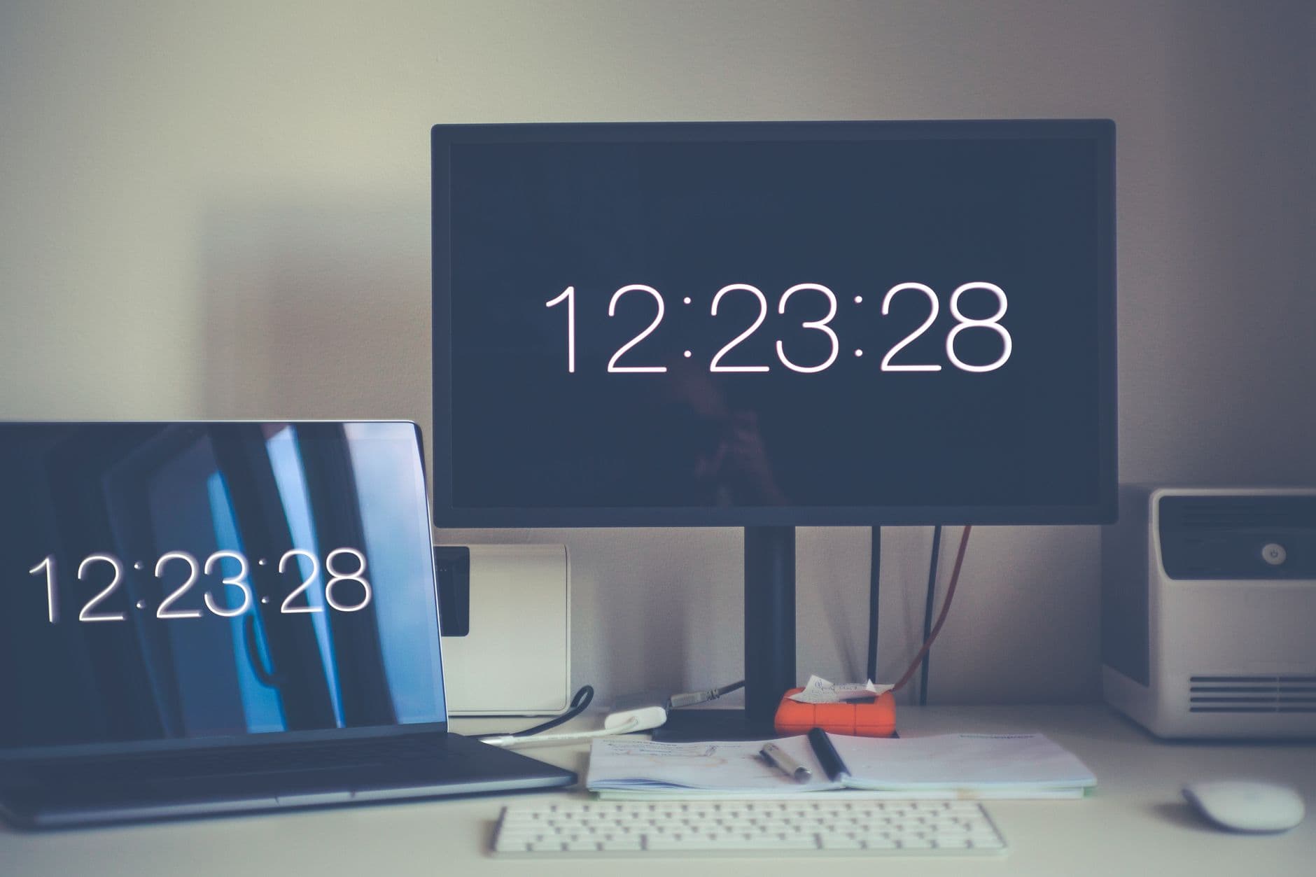 A contemporary desk setup featuring a laptop and monitor with digital clock displays.