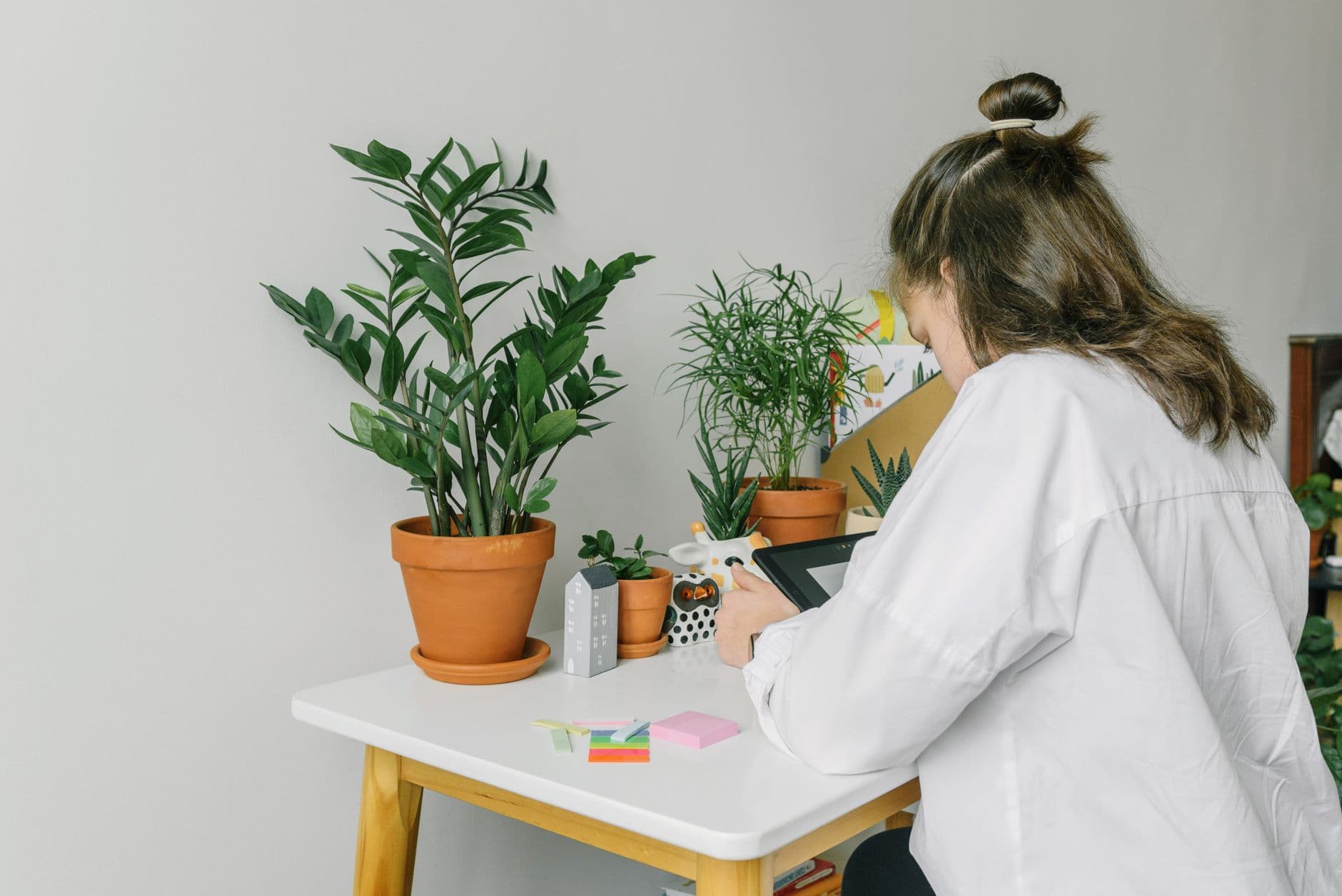 A young girl learns online surrounded by potted plants, adding a natural touch to her home study space.