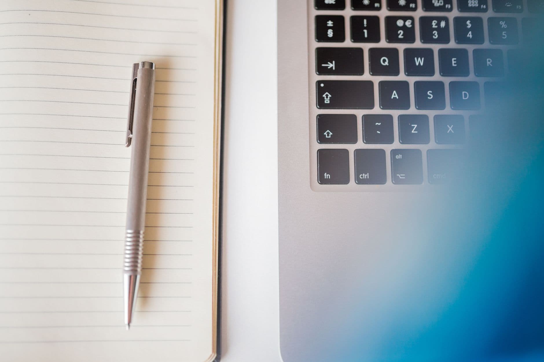 Simple workspace setup featuring a laptop keyboard and a notebook with a pen.