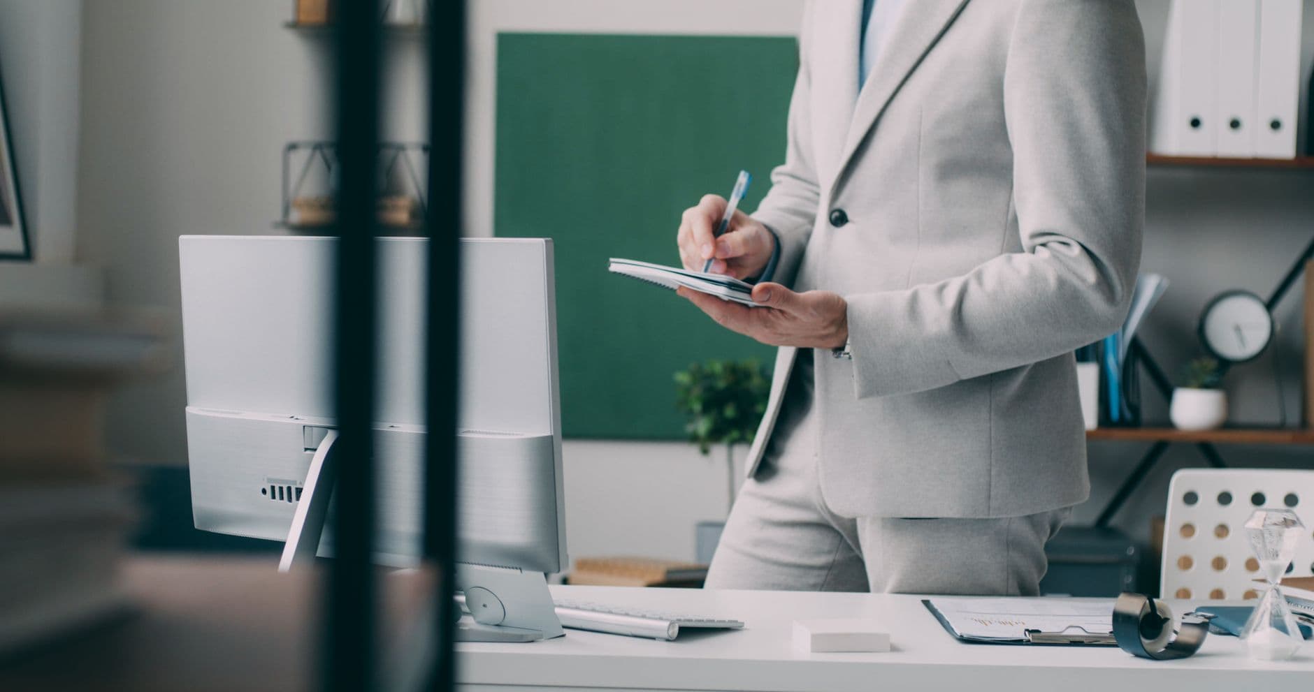 A focused businessman in a modern office, taking notes in front of a computer.